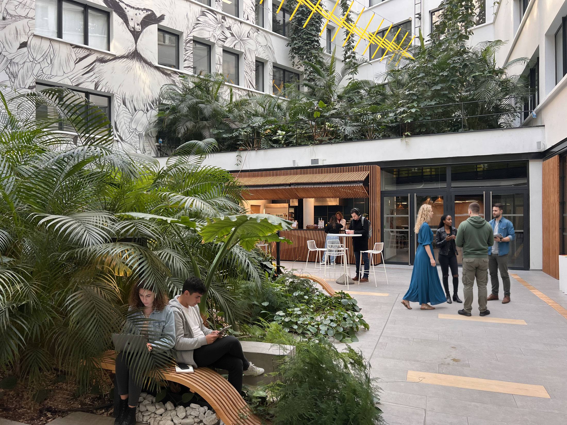 Espace de travail et de convivialité à Gambetta Village, Paris 20e, avec végétation luxuriante et habitants échangeant dans une cour urbaine moderne.